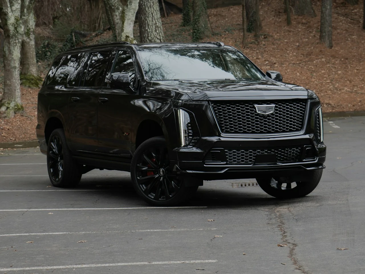 Full exterior of a black Cadillac Escalade, photographed from the front three-quarter angle with the entire vehicle and wheels visible