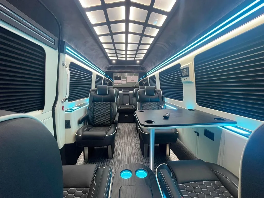 Photograph of a van cabin with black leather seats, tables and blue lighting